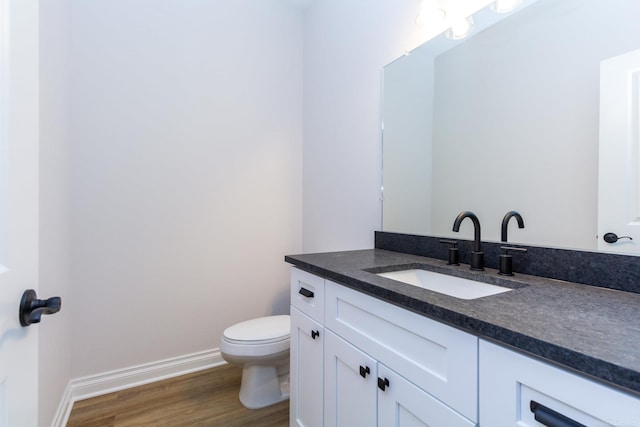 half bathroom with toilet, baseboards, wood finished floors, and vanity