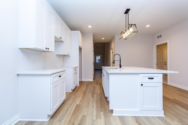 kitchen with white cabinets, an island with sink, light wood-style flooring, a sink, and recessed lighting