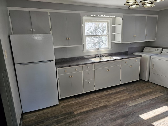 kitchen with dark wood-type flooring, a sink, freestanding refrigerator, dark countertops, and washing machine and clothes dryer