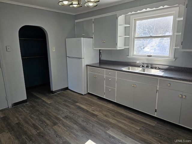 kitchen with arched walkways, dark countertops, a sink, and freestanding refrigerator