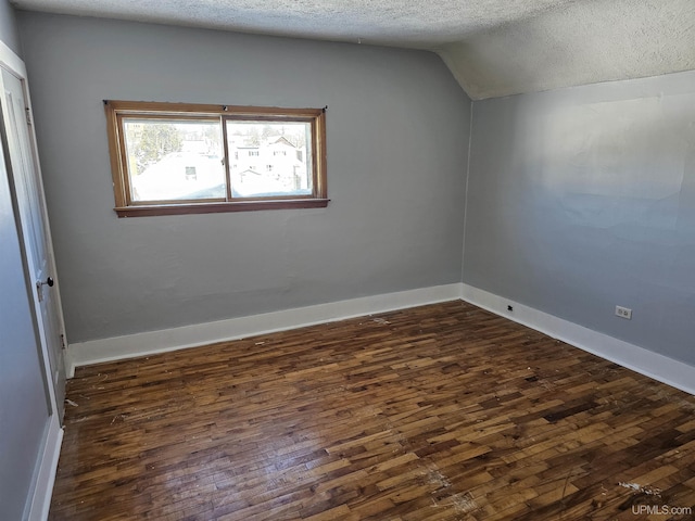 unfurnished room with lofted ceiling, dark wood-style flooring, a textured ceiling, and baseboards