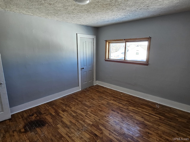 spare room featuring a textured ceiling, baseboards, and dark wood-type flooring