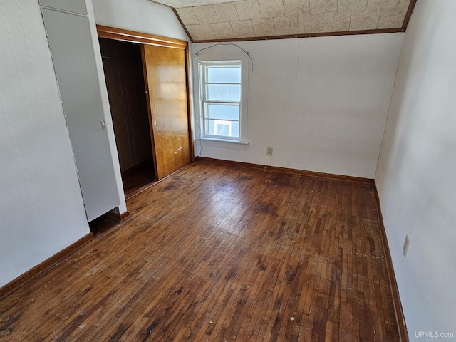 unfurnished bedroom featuring lofted ceiling, hardwood / wood-style flooring, baseboards, and a closet