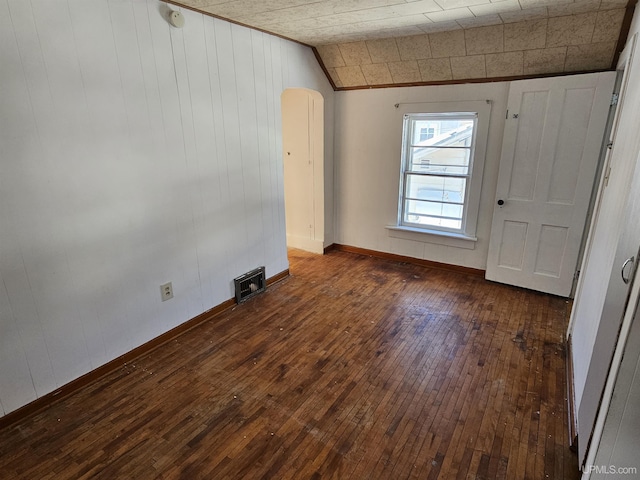 empty room with baseboards, visible vents, arched walkways, lofted ceiling, and dark wood-style floors