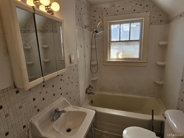 bathroom featuring bathtub / shower combination, toilet, a sink, tile walls, and vaulted ceiling