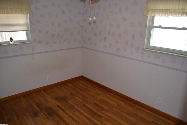 unfurnished room featuring wallpapered walls, wood-type flooring, baseboards, and wainscoting