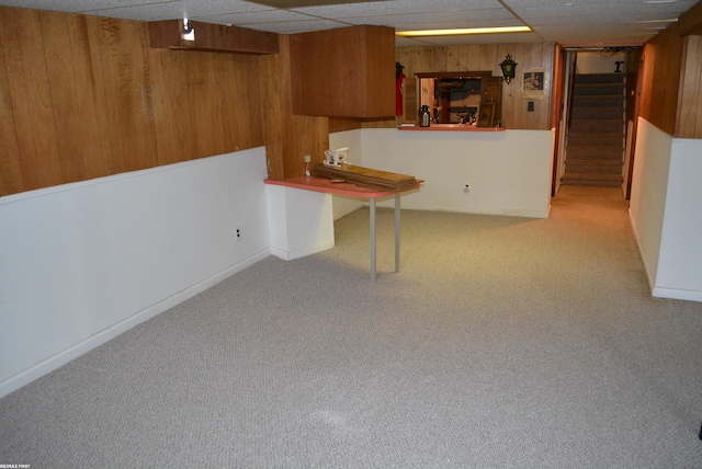 finished below grade area featuring a paneled ceiling, stairs, wooden walls, and carpet floors