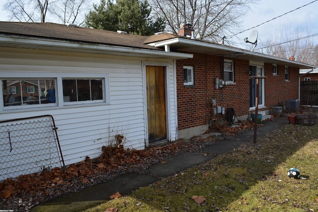 view of front facade featuring central AC, brick siding, a chimney, and fence