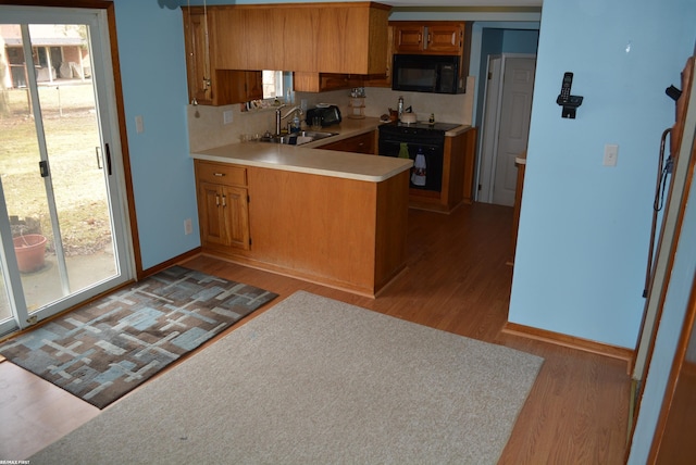 kitchen featuring brown cabinets, light countertops, light wood-style floors, a peninsula, and black appliances