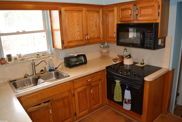 kitchen featuring brown cabinetry, light countertops, a sink, and black appliances