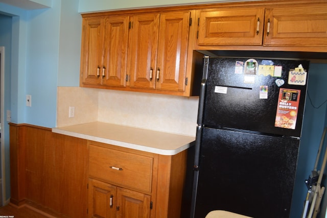 kitchen featuring wainscoting, brown cabinetry, light countertops, and freestanding refrigerator