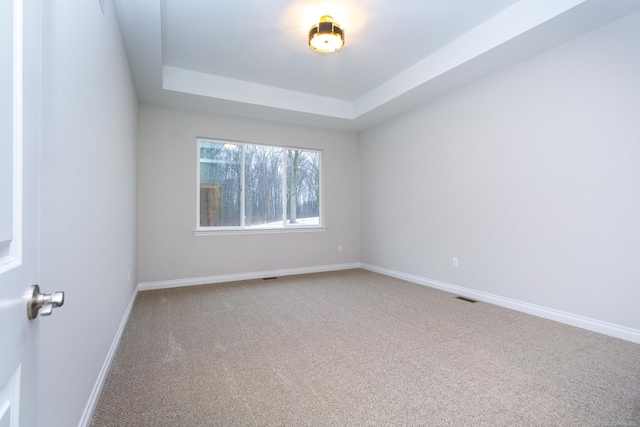 carpeted spare room featuring baseboards, visible vents, and a tray ceiling