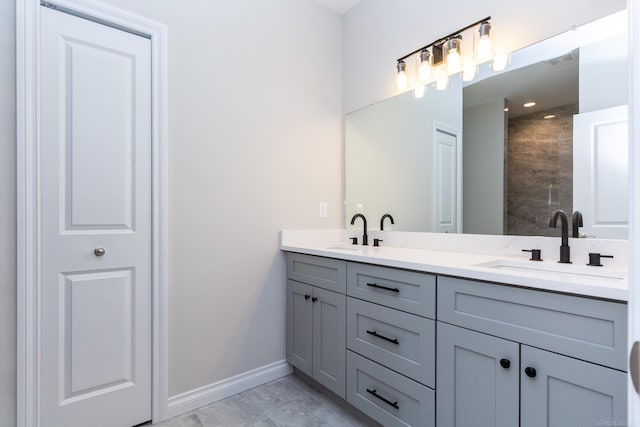 full bath with double vanity, baseboards, a tile shower, and a sink