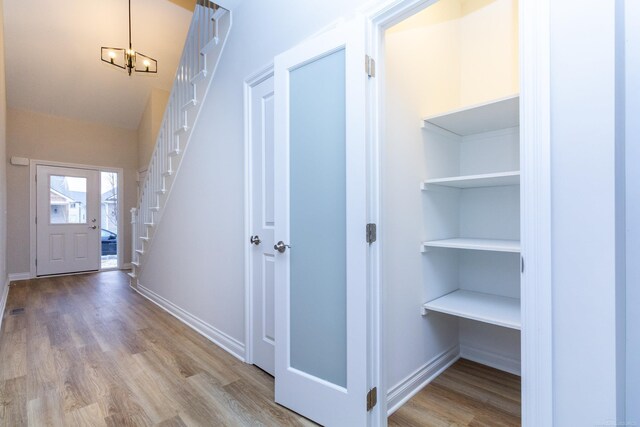 entrance foyer with stairs, a notable chandelier, baseboards, and wood finished floors