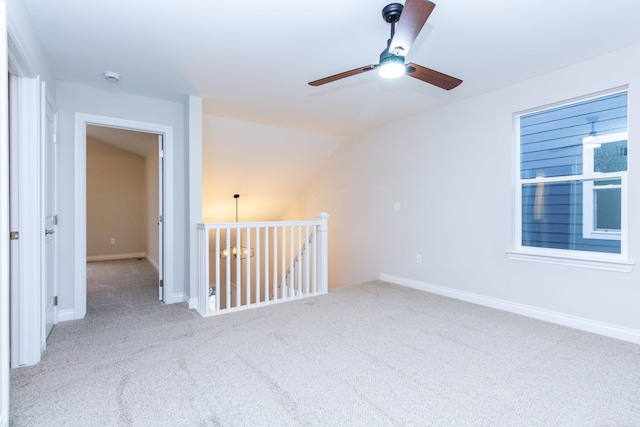 carpeted empty room with vaulted ceiling, a ceiling fan, and baseboards