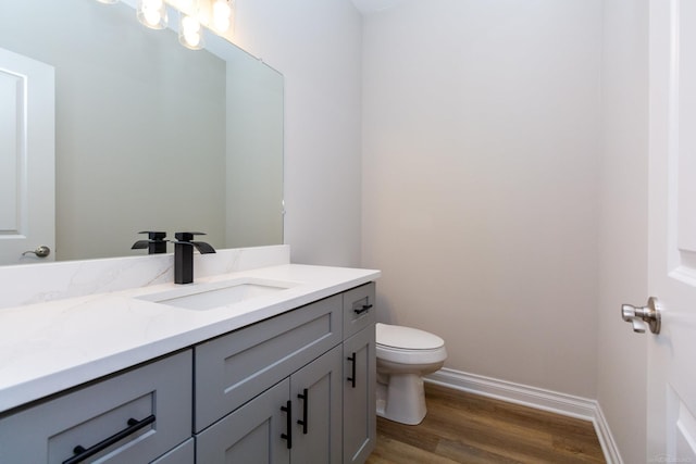 bathroom with baseboards, toilet, wood finished floors, an inviting chandelier, and vanity