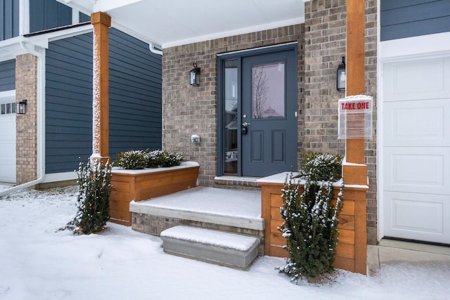 snow covered property entrance with brick siding, board and batten siding, and an attached garage