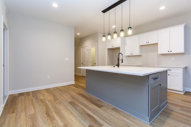 kitchen with recessed lighting, white cabinets, light countertops, light wood-type flooring, and an island with sink