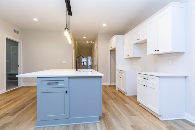 kitchen featuring a kitchen island with sink, a sink, visible vents, and white cabinets