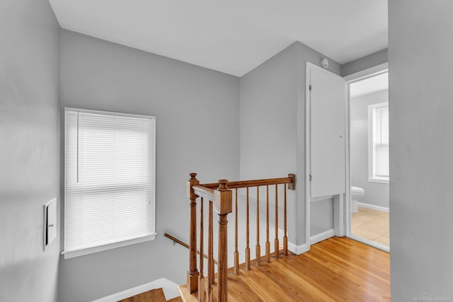 corridor featuring baseboards, an upstairs landing, and wood finished floors