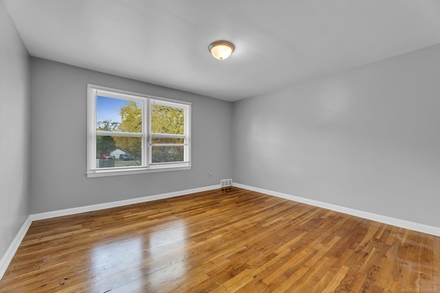 spare room with hardwood / wood-style floors, visible vents, and baseboards