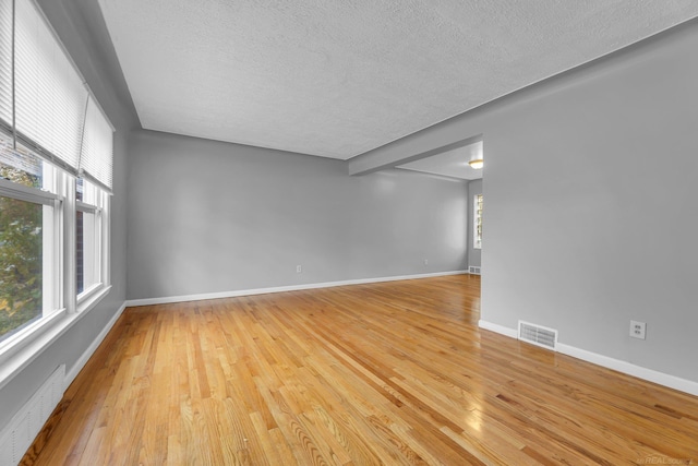 spare room featuring light wood-style floors, visible vents, a textured ceiling, and baseboards