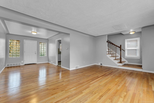 unfurnished living room with stairs, hardwood / wood-style flooring, visible vents, and baseboards