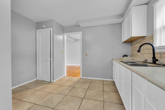 kitchen featuring white cabinetry, a sink, backsplash, and light tile patterned floors