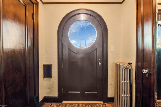 entrance foyer featuring crown molding, radiator, a textured wall, and baseboards