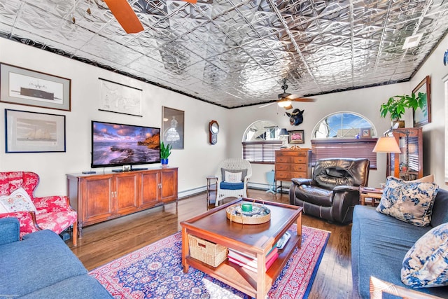 living area featuring an ornate ceiling, baseboard heating, wood-type flooring, and a ceiling fan