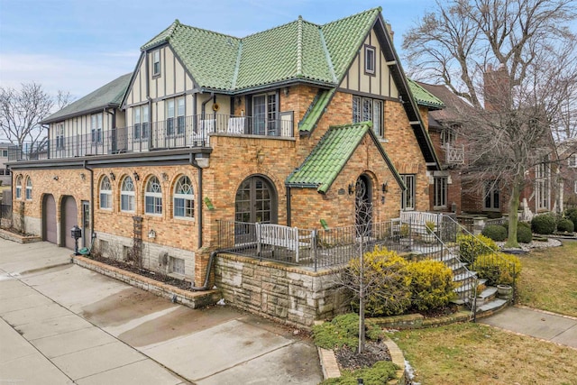 view of front of home featuring driveway, brick siding, a tiled roof, and a balcony