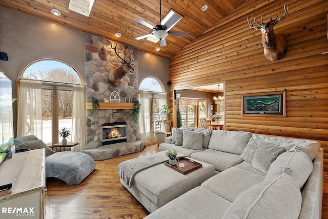 living area featuring wooden ceiling, hardwood / wood-style floors, a stone fireplace, high vaulted ceiling, and ceiling fan with notable chandelier