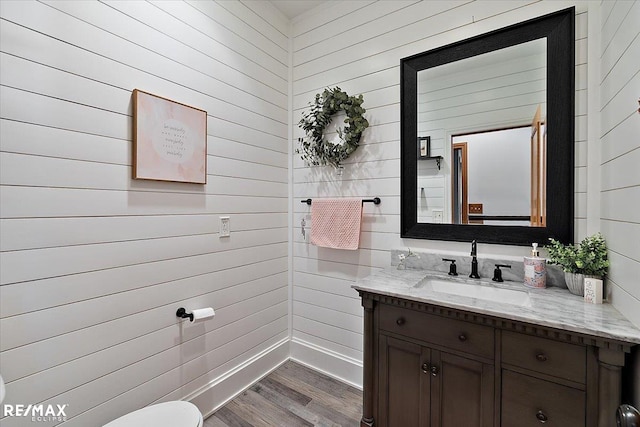 half bathroom with toilet, vanity, baseboards, and wood finished floors