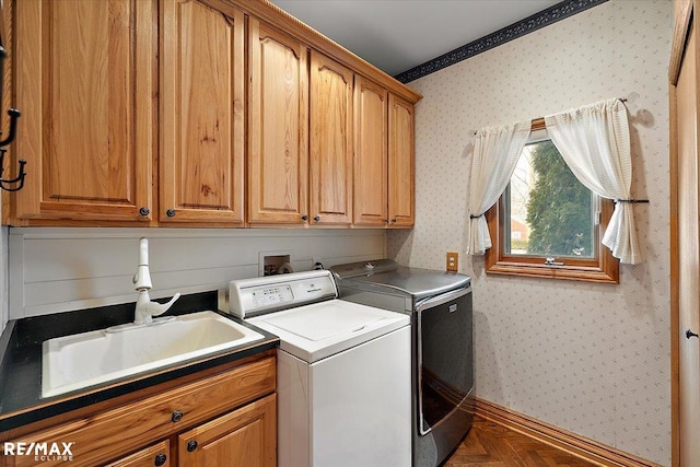 washroom with a sink, wallpapered walls, cabinet space, and washer and dryer