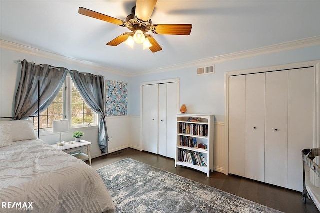 bedroom with visible vents, ceiling fan, wood finished floors, crown molding, and two closets