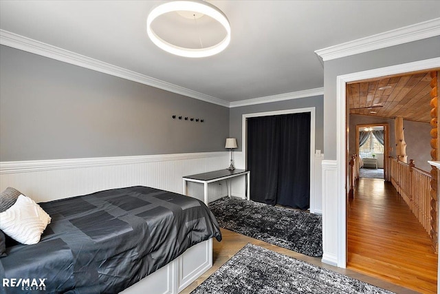 bedroom with wood finished floors, crown molding, and wainscoting