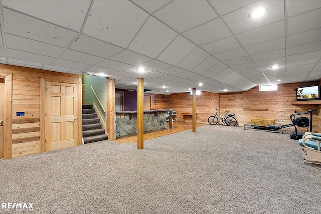 finished below grade area featuring a paneled ceiling, carpet, wooden walls, and stairway