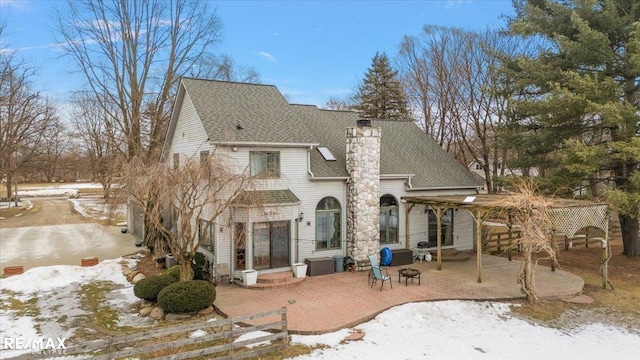 rear view of house featuring entry steps, roof with shingles, a chimney, and a patio area