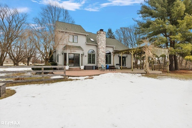 snow covered back of property featuring fence, a chimney, and a patio