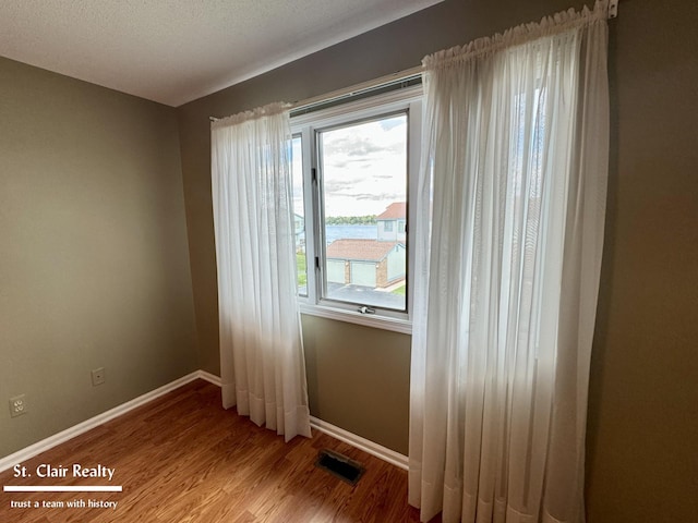 empty room featuring wood finished floors, visible vents, and baseboards