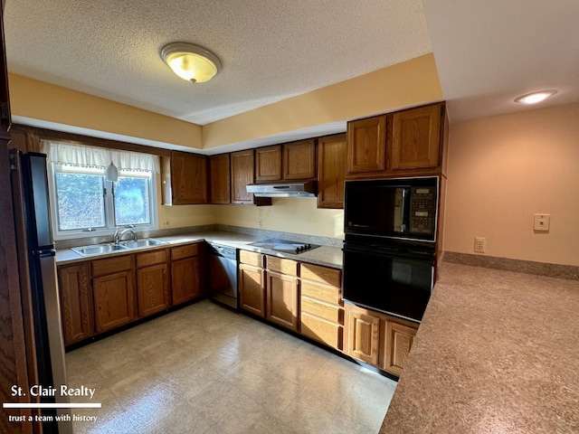 kitchen with brown cabinetry, under cabinet range hood, light countertops, black appliances, and a sink