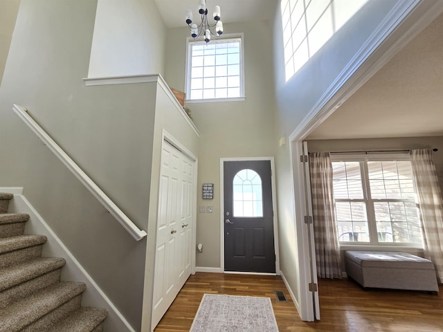 foyer with wood finished floors, visible vents, baseboards, stairway, and an inviting chandelier