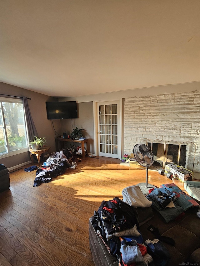 living area featuring a stone fireplace, baseboards, and hardwood / wood-style floors