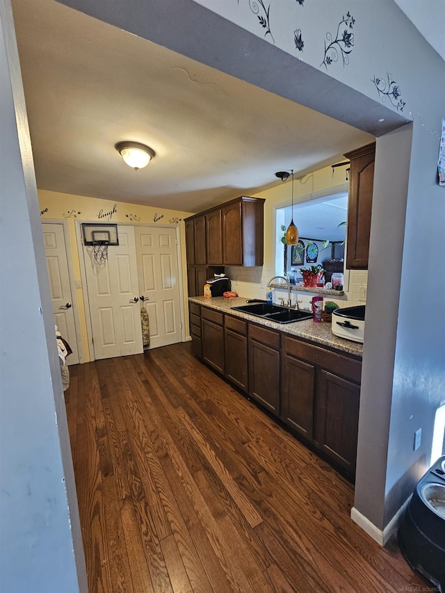 kitchen featuring a sink, dark wood finished floors, decorative backsplash, dark brown cabinets, and hanging light fixtures