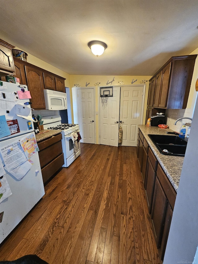 kitchen featuring a sink, white appliances, dark wood-type flooring, and dark brown cabinetry