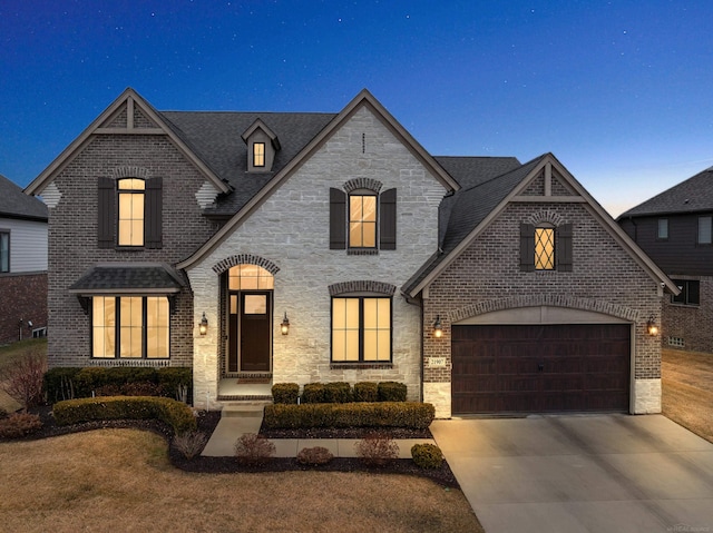 french country style house with stone siding, brick siding, driveway, and an attached garage