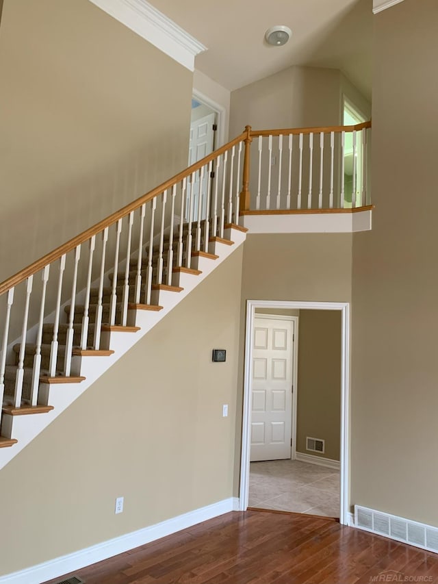 staircase featuring visible vents, a towering ceiling, baseboards, and wood finished floors