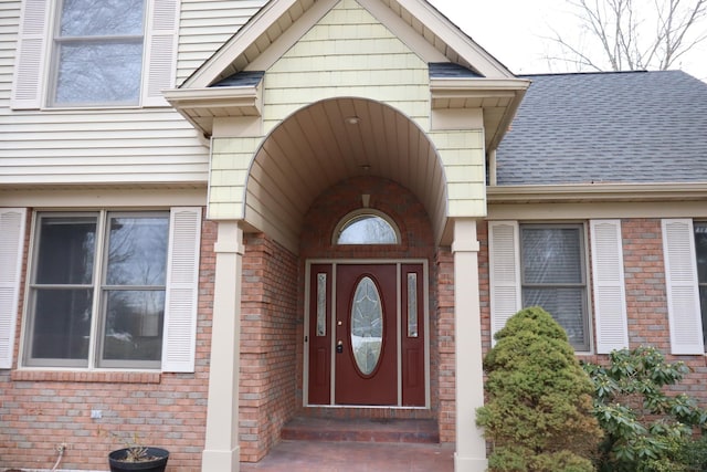 doorway to property with roof with shingles and brick siding