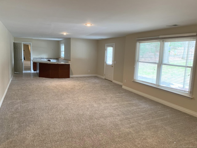 unfurnished living room with visible vents, light carpet, and baseboards