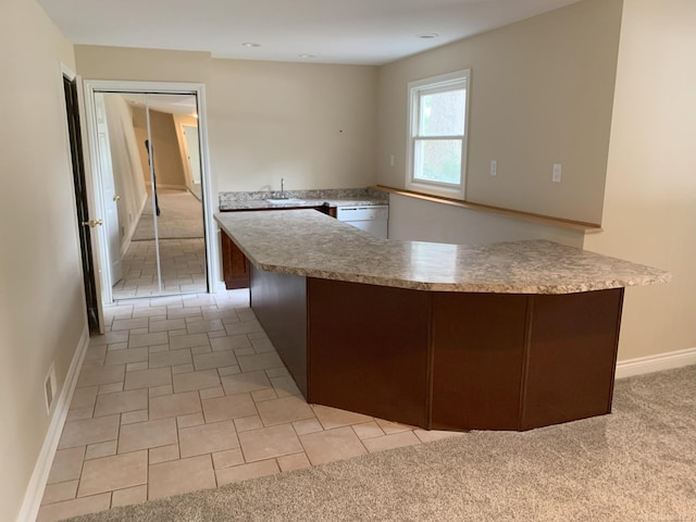 kitchen featuring white dishwasher, light colored carpet, a sink, baseboards, and light countertops